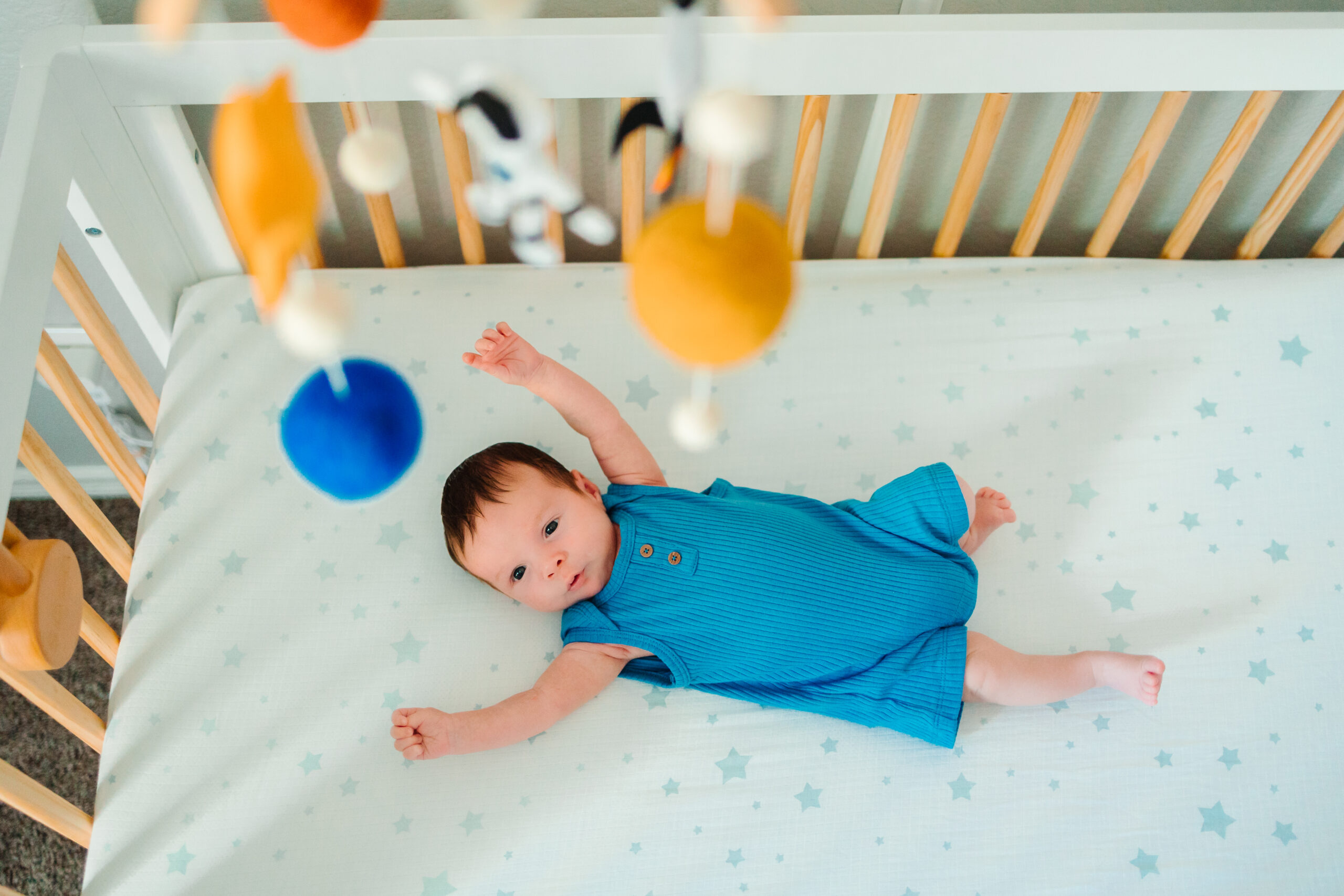 baby boy lying awake in crib looking up at outer space themed mobile