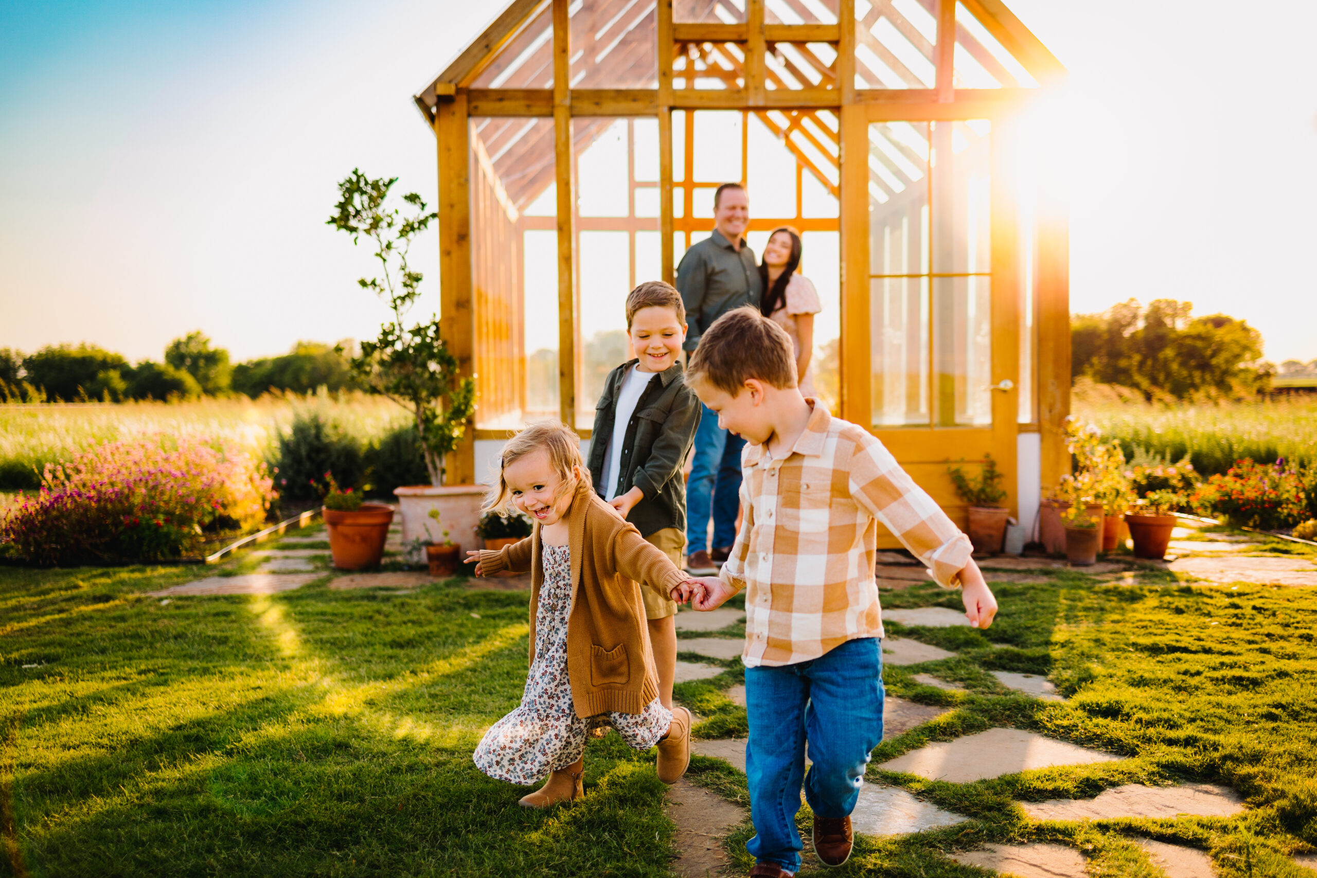 Family with 3 kids running in front of a greenhouse with sunflare