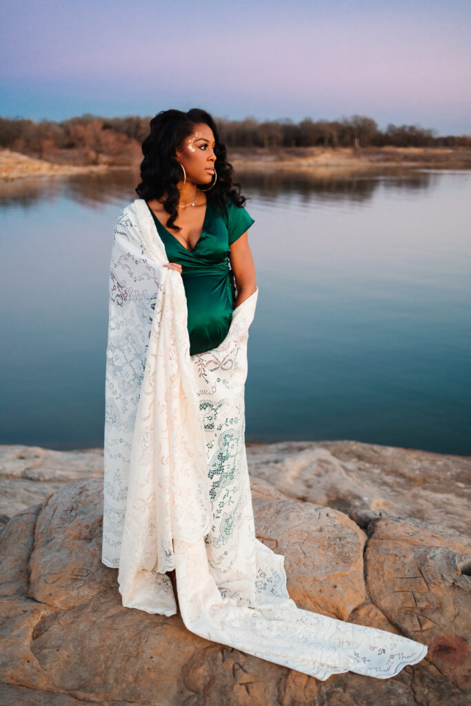 pregnant woman wrapped in a blanket standing in front of a lake at sunset