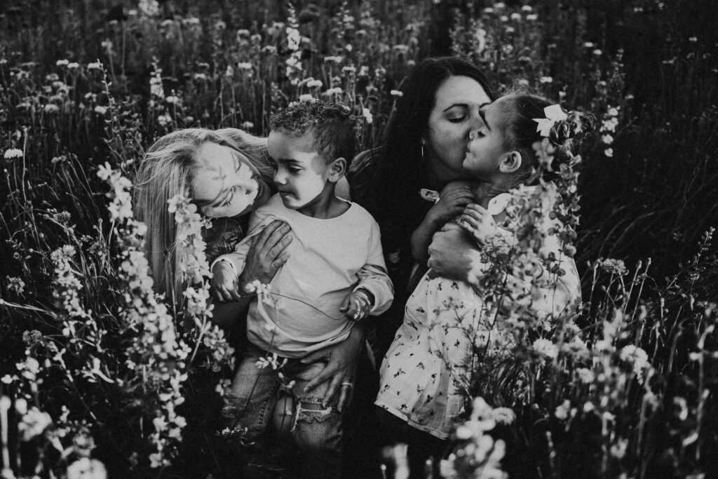 black and white image of an lgbt family. The two moms are snuggling with their twin toddlers in a field of wildflowers.