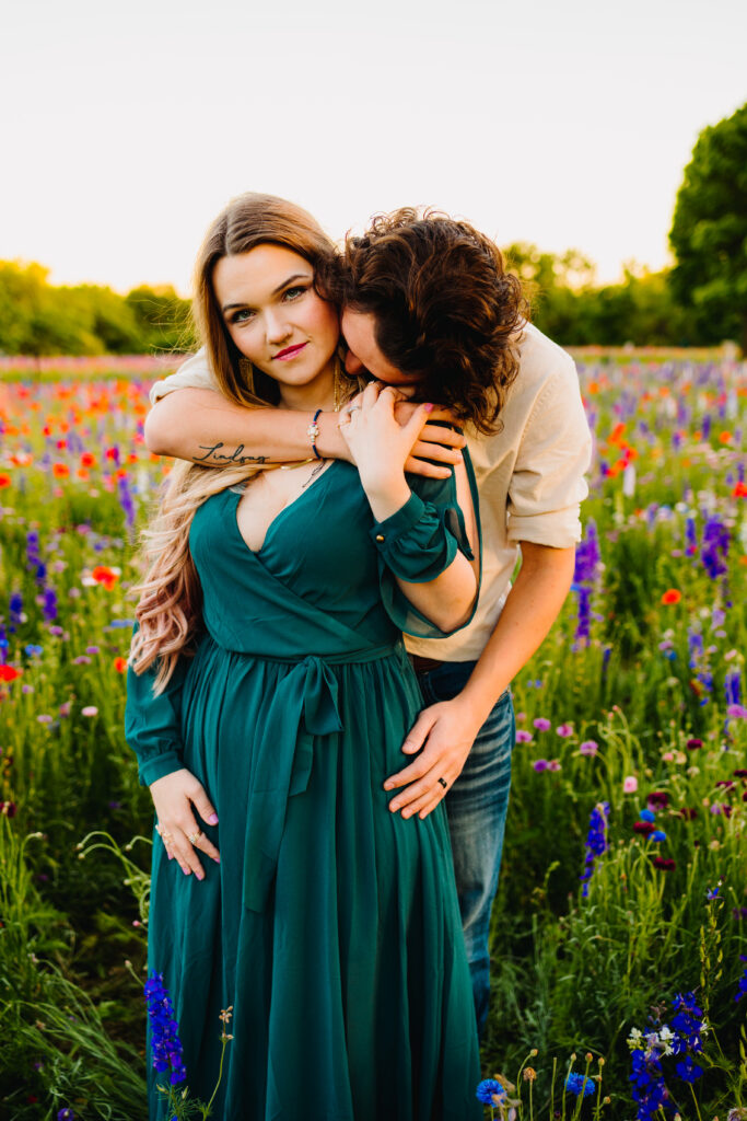 couple embracing during a wildflower mini session in dfw texas. The dad is kissing the mom's neck and the mom is looking at the camera