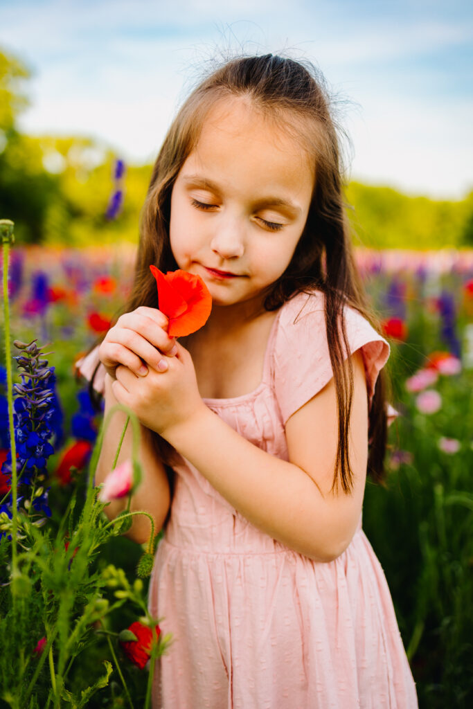 young girl smelling a poppy in a wildflower field in dallas