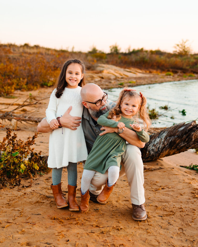 father and two daughters playing on the beach during a family photo session with wandermama photography at murrell park in flower mound tx